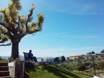 Man by tree against blue sky