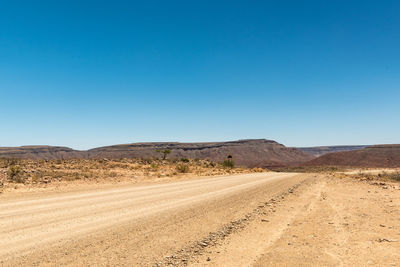 Dirt road passing through desert against clear blue sky