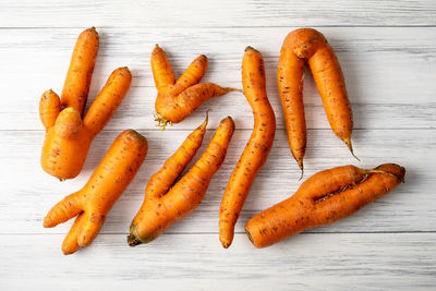 Top view close-up of several ripe orange ugly carrots lie on a light wooden surface. 