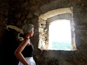 Side view of mature woman looking through window while standing in old building