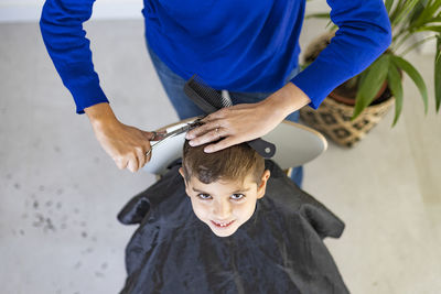 Funny boy getting haircut at home with scissors