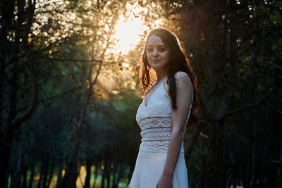 Young woman standing by tree in forest