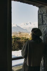 Rear view of woman looking at distance leaning in window