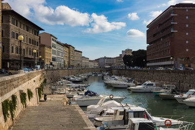 Boats moored in canal amidst buildings in city against sky