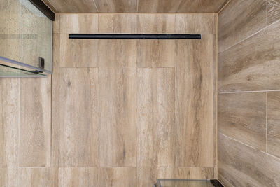 Modern black linear drain in a bathroom lined with ceramic tiles imitating wood, top view.