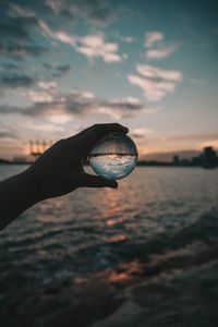 Close-up of hand holding crystal ball against sea at sunset