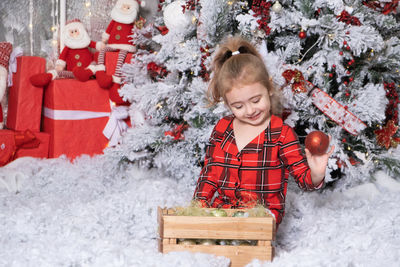 Cute little girl playing with christmas balls in christmas decorated room. merry christmas concept