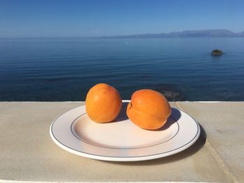 Orange fruits in plate on table by sea against sky