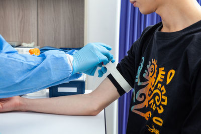 Nurse tightening the elastic band on a male patient arm to collect a blood sample from in a clinic