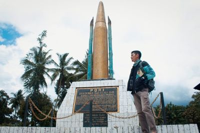 Low angle view of man standing by palm tree against sky