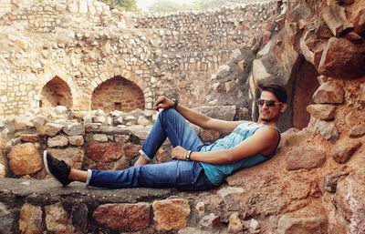 Young man sitting on rock against wall