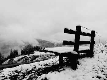 Cross on snow covered landscape against sky