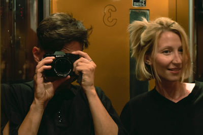 Mid adult man photographing woman reflecting on mirror in elevator