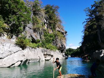 Young man on paddling wooden raft in river