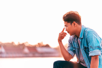 Young man looking away while sitting against clear sky