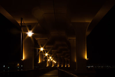Illuminated street lights under bridge at night