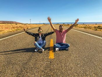 Portrait of cheerful couple sitting on road against clear blue sky