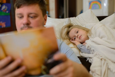 Dad entertains the child during illness, he looks, reads a book, a photo book with his daughter home