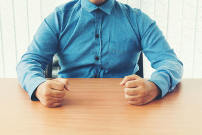 Midsection of businessman wearing blue shirt sitting at desk in office