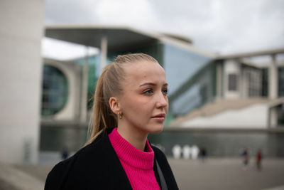 Smiling young woman looking away while standing against building