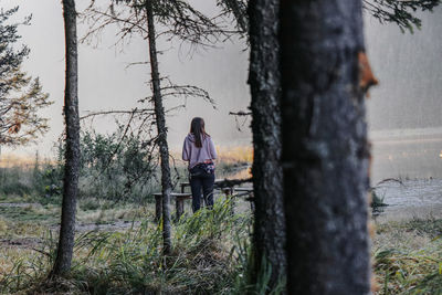 Woman standing by tree trunk in forest