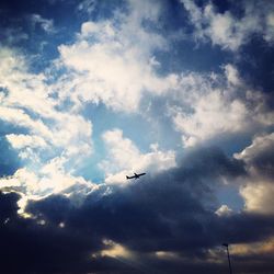 Low angle view of silhouette airplane flying against cloudy sky during sunset