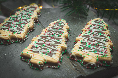 Three cookies in the shape of a christmas tree  and colored sprinkles balls  on a wooden cutting