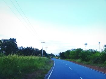 Road by electricity pylon against sky