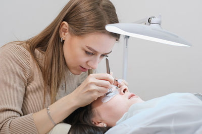 Woman beautician holding tweezers with false lash during lash extension procedure 