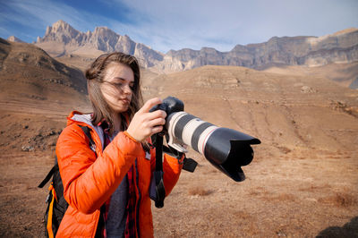 Young hipster woman with a camera in her hands in the mountains in backlight. hair fluttering 