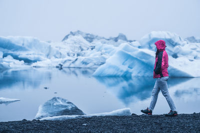 Person standing by frozen lake against sky