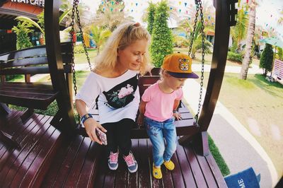 Mother and daughter sitting on swing in yard