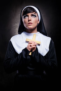 Nun holding cross while standing against black background