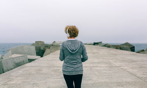 Rear view of woman standing by sea against clear sky