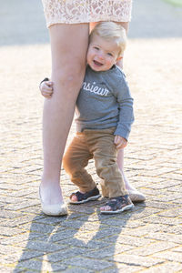 Sad caucasian blonde little boy hugging his mother legs