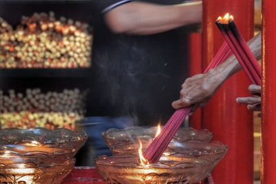 Cropped hands burning incense sticks on temple