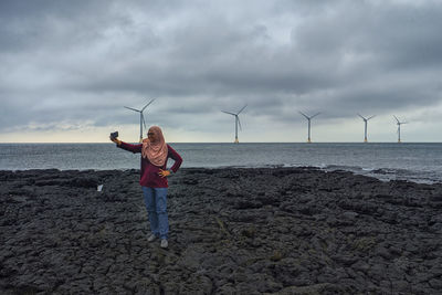 A muslim woman in hijab is taking a selfie with the windmill as background