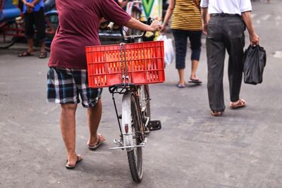 Vendor with crate on bicycle walking with people on street
