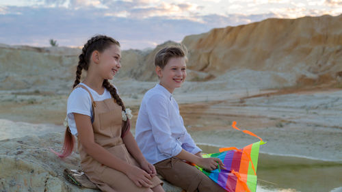 Portrait of smiling friends sitting on rock