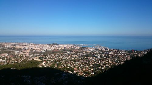 Aerial view of townscape by sea against clear blue sky