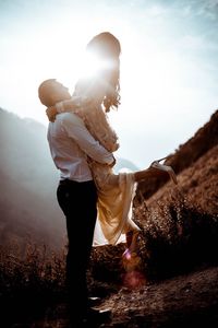 Man and woman standing on field against sky during sunset