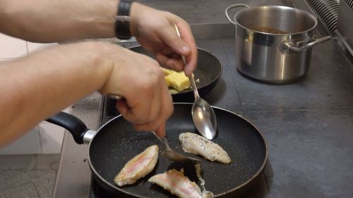 Cropped image of man frying fish in saucepan at kitchen counter