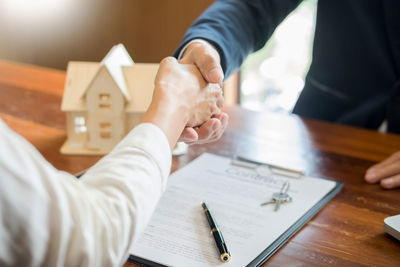 Midsection of client and businessman handshaking above contract paper on table