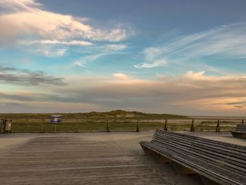 Empty benches on footpath against sky during sunset