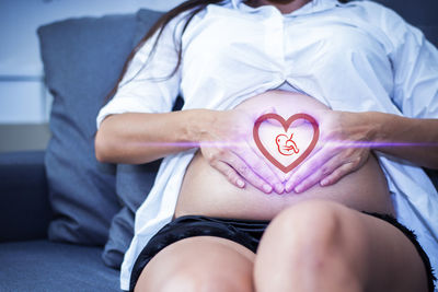 Digital composite image of pregnant woman making heart shape with baby symbol on stomach