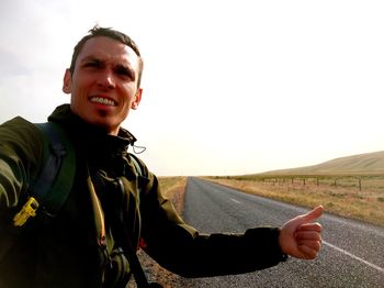 Smiling man hailing ride while standing on road against sky