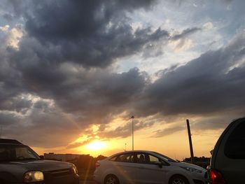 Vehicles on road against cloudy sky at sunset