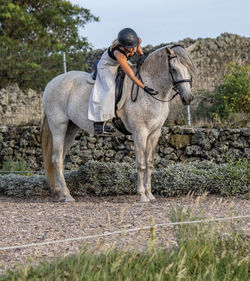 White lusitano mare, female dressage rider, outdoors on sand.