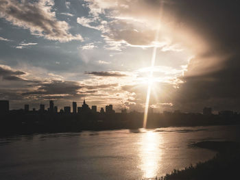 Silhouette buildings by sea against sky during sunset