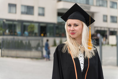 Portrait of woman wearing graduation gown standing against building